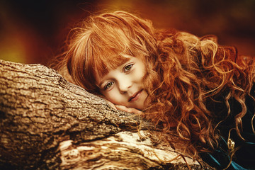 beautiful little girl with red hair and a bow and arrows in the green forest