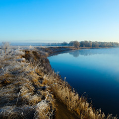 Coast with grass covered with frost. River with morning fog.