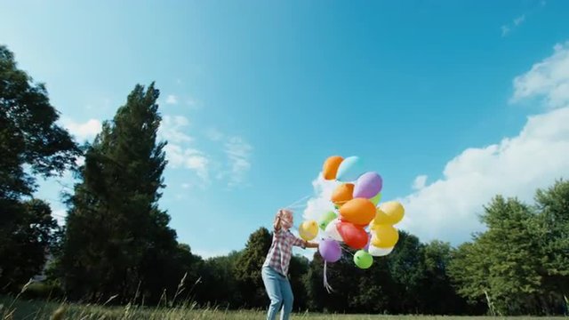 Girl letting go balloons flying in the sky. Happy child waving hand