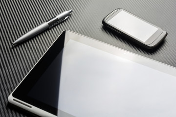 Blank Business Smartphone And A Pen Lying Next To A Tablet With Reflection Above A Carbon Background