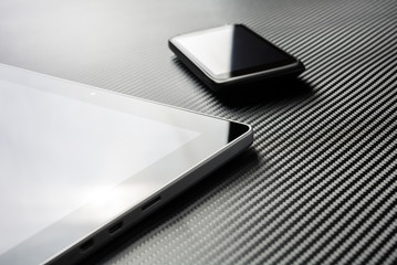 Business Smartphone With Reflection Lying Next To Blank Tablet On A Carbon Layer