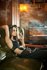 Young beautiful brunette woman in black male  trousers, hat and braces relaxing on a sofa in vintage scenery. 