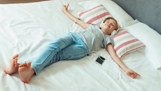 Girl listening music in headphones and lying on the bed