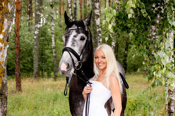 Obraz premium Beautiful blonde woman and gray horse in forest