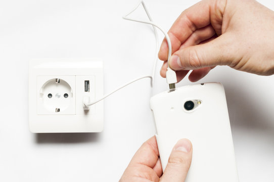 Charging. A man plugs  the smartphone to the socket, with two us