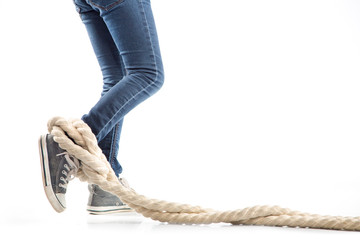Woman legs in jeans and sneakers entangled rope on white background. Concept of restrictions