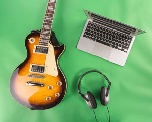 Electric guitar with laptope and headphones on green background