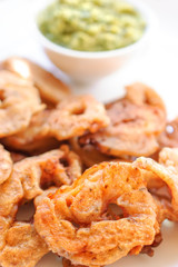 Rings of a squid fried in batter with green sauce on a white plate.