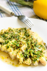 White fish fillet baked with herbs and spices on a white plate.