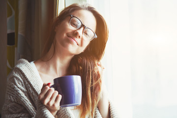 cheerful girl drinking coffee or tea in morning sunlight near wi