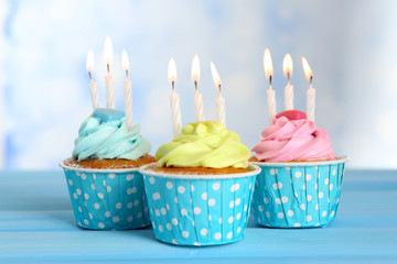 Delicious cupcakes with candles on blue wooden table against blurred background