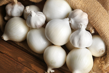 Scattered bag with onions and garlic on wooden background