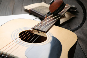 Acoustic guitar, headphones, musical notes and white papers on wooden background, close up