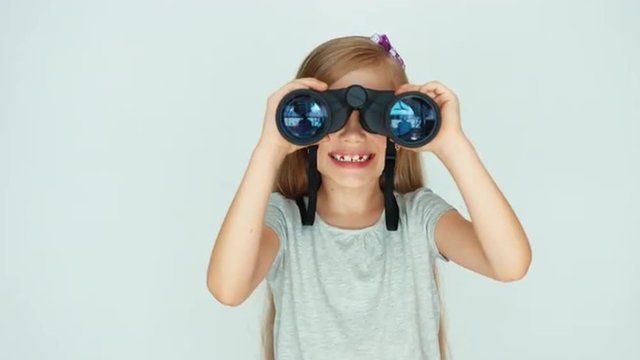 Girl looking through binoculars at camera. Girl laughing on a white background