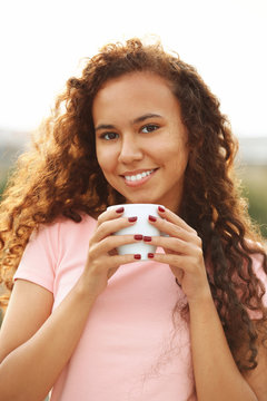 Close up portrait of pretty young woman in pink dress drinking coffee at summer terrace