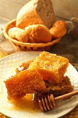 Honeycombs on plate, hot buns in basket on wooden background