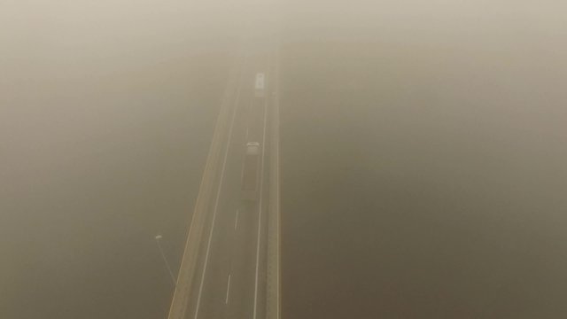 4K aerial view – flight over misty morning bridge showing road vehicles moving forward up