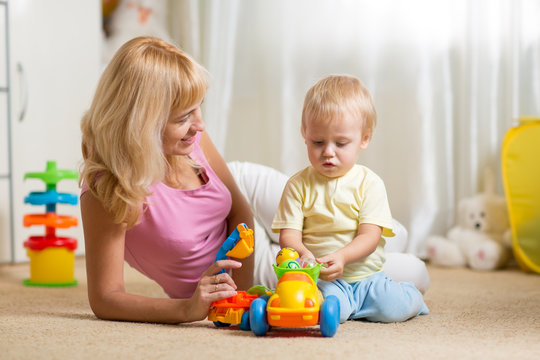 Mother and toddler son play with toy car on nursery floor