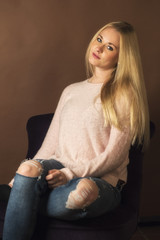 Blonde junge Frau in Jeans sitzt auf einem Sessel