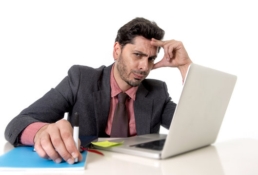 attractive businessman at office desk working on computer laptop looking tired and busy