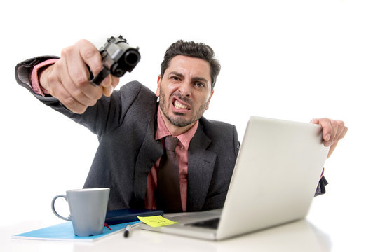businessman at office desk working on computer laptop pointing gun looking angry and crazy
