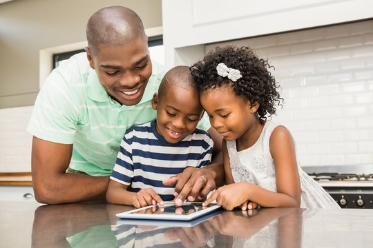 Father Using Tablet With His Children In Kitchen