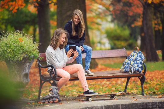 Two young girl watching tablet in the park after skateboarding