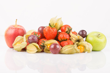 Red and green apples with orange physalis, purple grapes and red strawberries on white background.