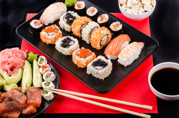 Sushi set, soy sauce, ginger, wasabi, black and red roe, avocado, salmon, cheese on black and red background.