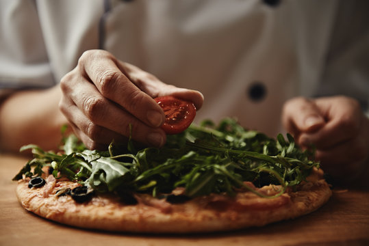 Female baker preparing pizza with ham, arugula and cherry tomatoes. Mediterranean cuisine.