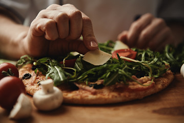 Baker hands putting parmesan cheese on pizza. Italian cuisine concept. - obrazy, fototapety, plakaty
