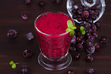 Frozen summer berries smoothie garnished with mint on dark wooden background