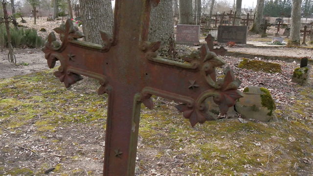 The view of the cemetery with the metal cross. Dried fallen leaves are found on the ground of the forest