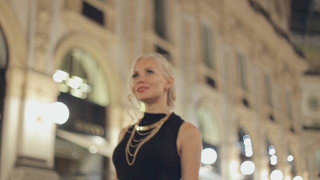 Happy woman in one of the world's oldest shopping malls, in Milan at night