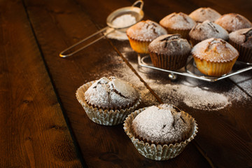 Muffins, caster sugar, sieve for a baking on a dark wooden background, selective focus