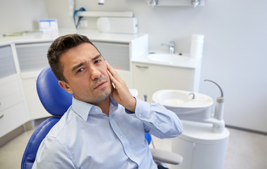 man having toothache and sitting on dental chair