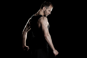 muscular man,  clasps hands in  fist, black background, place for text on the right