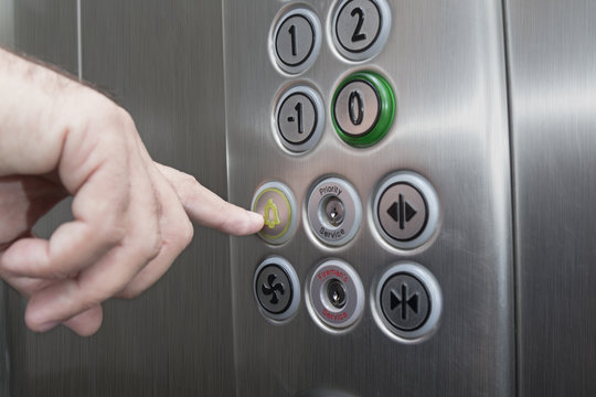 Forefinger pressing the alarm button in the elevator