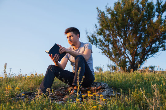 man sits on a hill with a book and looking away
