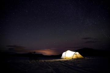 beleuchtetes Zelt im Winter in Schweden mit leichten Nordlichtern im Hintergrund