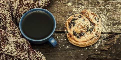 Coffee cup, scarf and sweet bun  on a wooden background.
