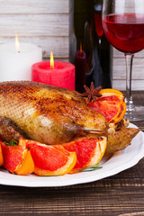 Festive Christmas duck baked with grapefruit and rosemary, glass and bottle of red wine; candles