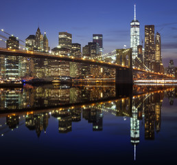 Fototapeta na wymiar Manhattan waterfront with Brooklyn Bridge reflected in water at night, NYC, USA.