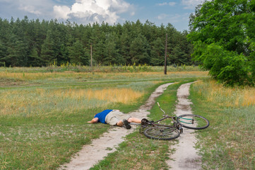 man lying on a country road after he fallen down from an ancient bicycle
