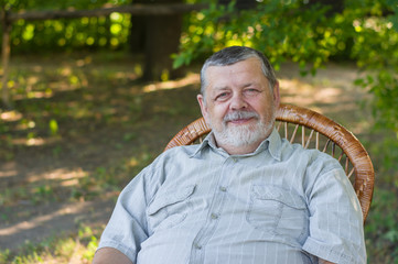 Outdoor portrait of a happy senior man sitting in a chair in summer park
