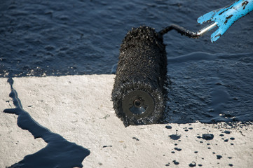 Roofer worker painting black coal tar or bitumen at concrete surface by the roller brush,  ...