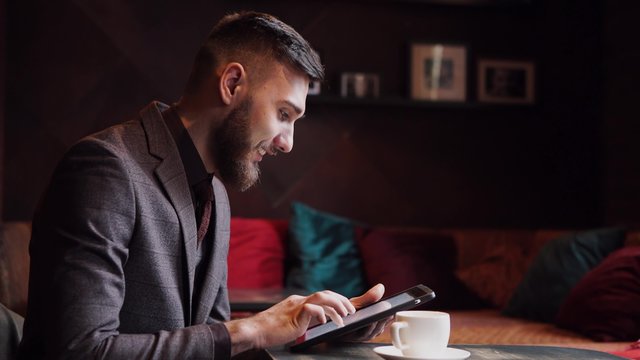 Nerd hipster guy sitting at bar table and using a tablet