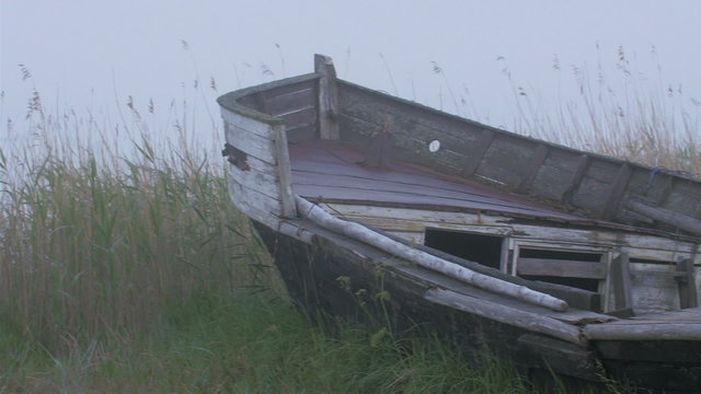 The abandoned ruined wooden boat on the ground. The boat is on the grassy area of the port