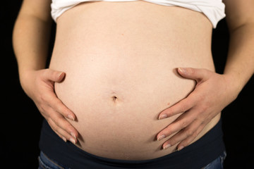 Junge Frau hält ihren Babybauch vor schwarzem Studiohintergrund