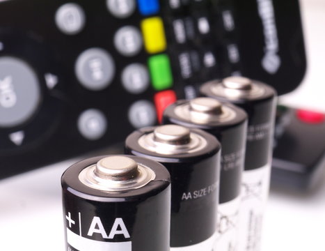 four AA batteries in a row in front of remote control, macro, shallow depth of field